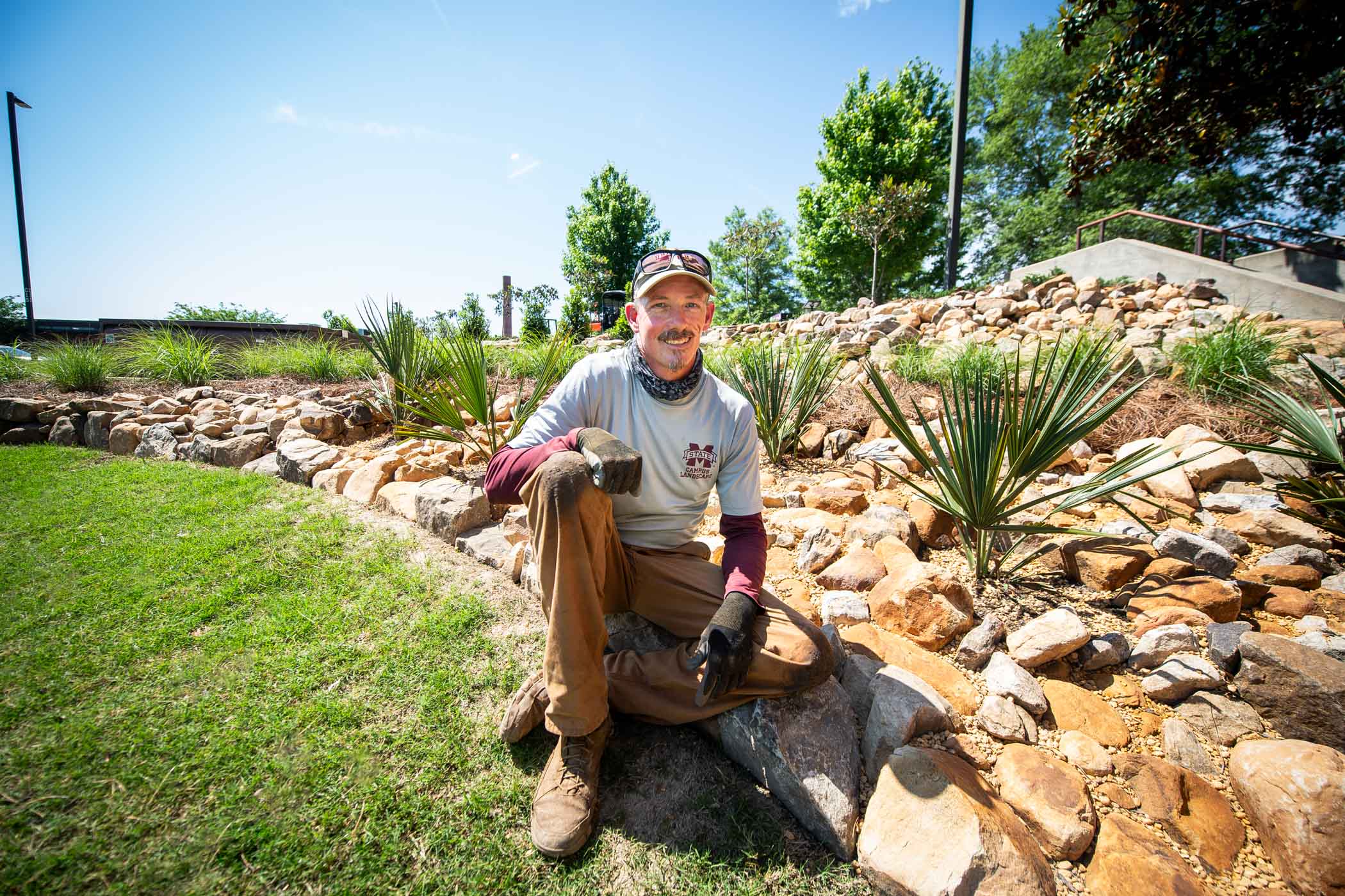 Dylan Karges, lead horticulture crew member for MSU Campus Landscape, sits among his latest installation of rocks, palms, and monkey-grass on the eastern side of Hilbun Hall. 