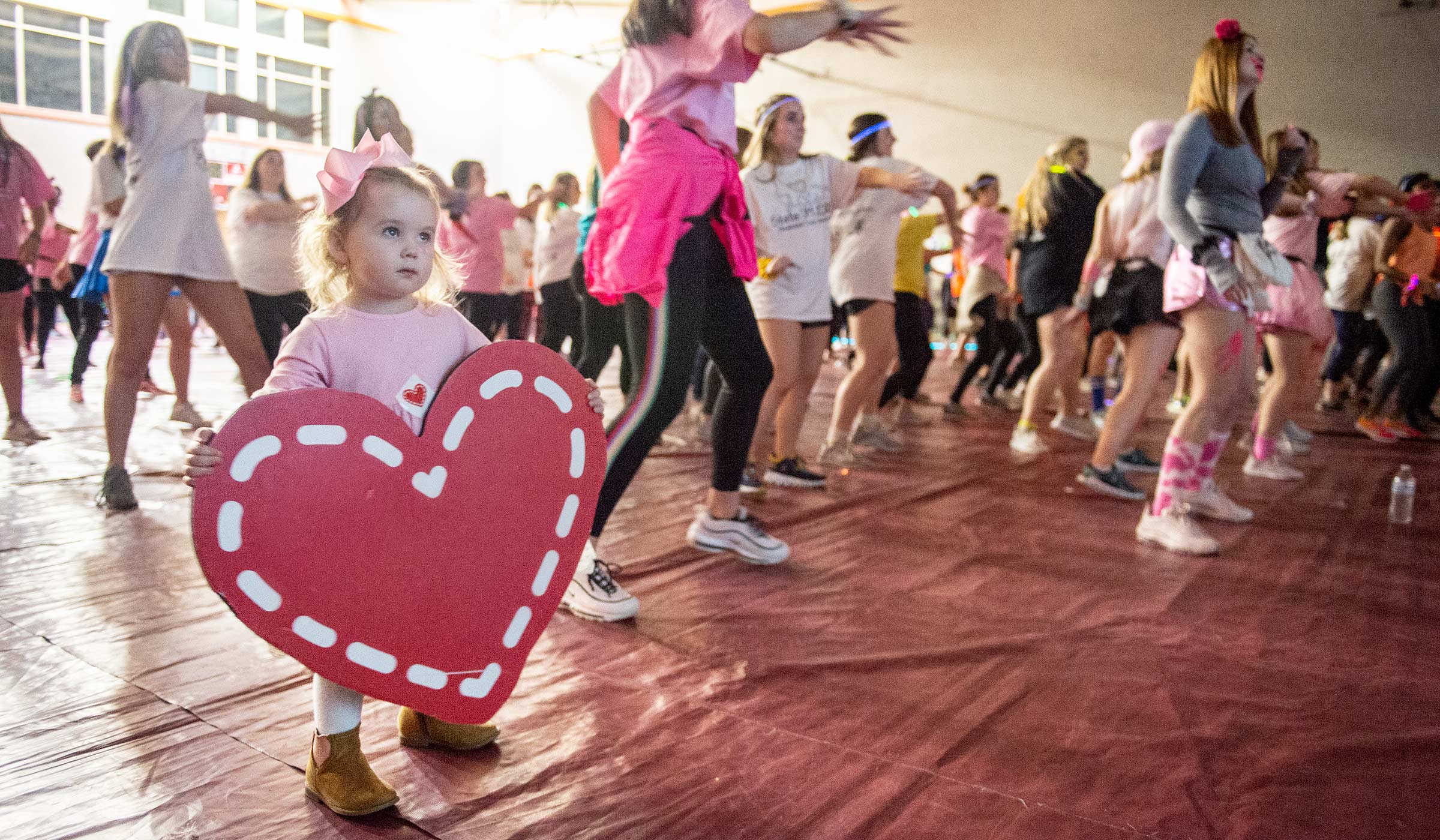 Two year old Mary Michael Kimbrough holds a Dance Marathon heart on the dance floor, while MSU students dance around her.