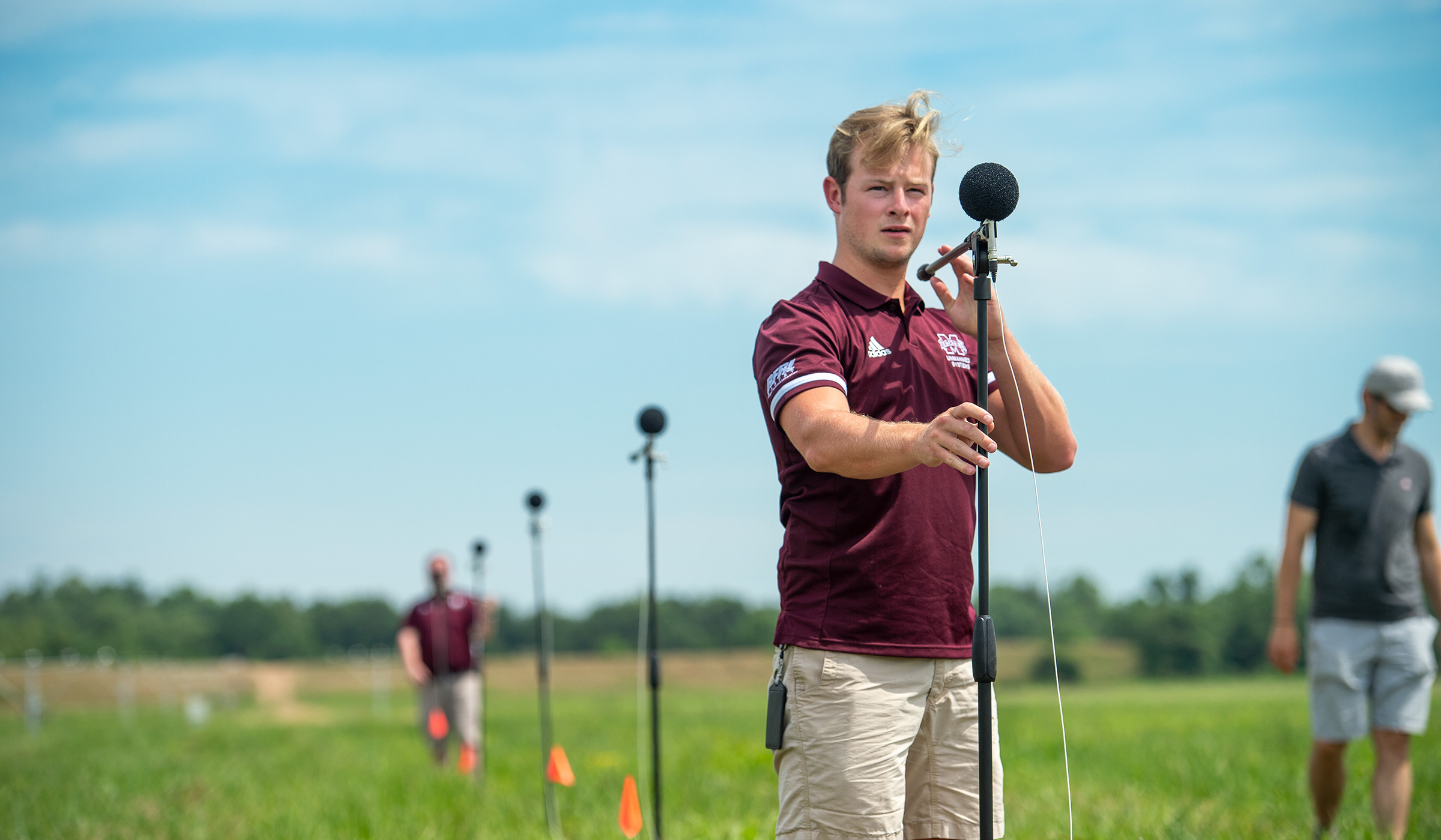 In the foreground of an array of microphones stretched out in a field ajacent to Greenwood-LeFlore Airport, a Raspet engineer in the foreground adjusts the microphone angle.