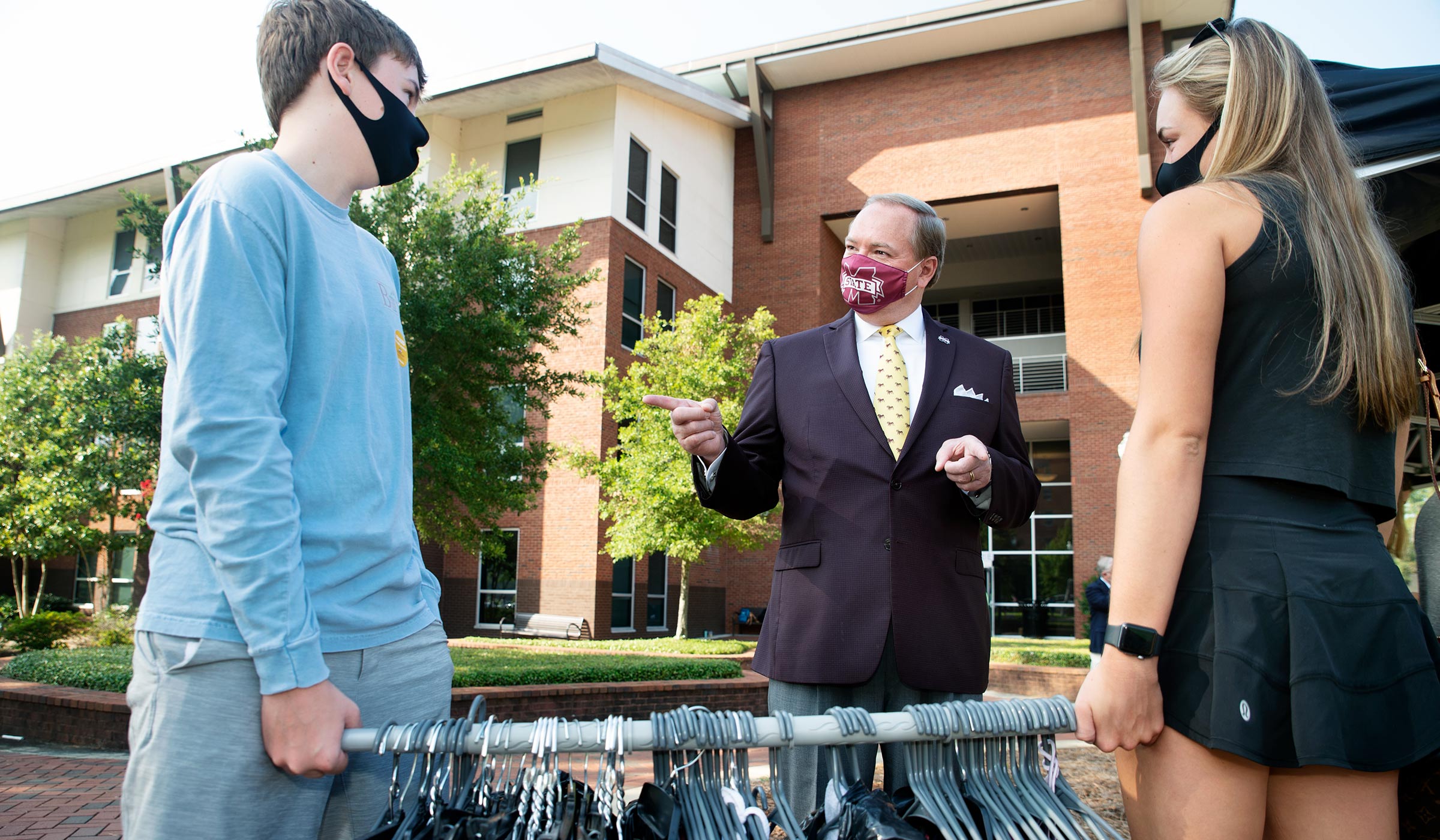 With Oak Hall behind them on Move-in Day, President Keenum speaks to a pair holding a rod filled with hanging clothes.