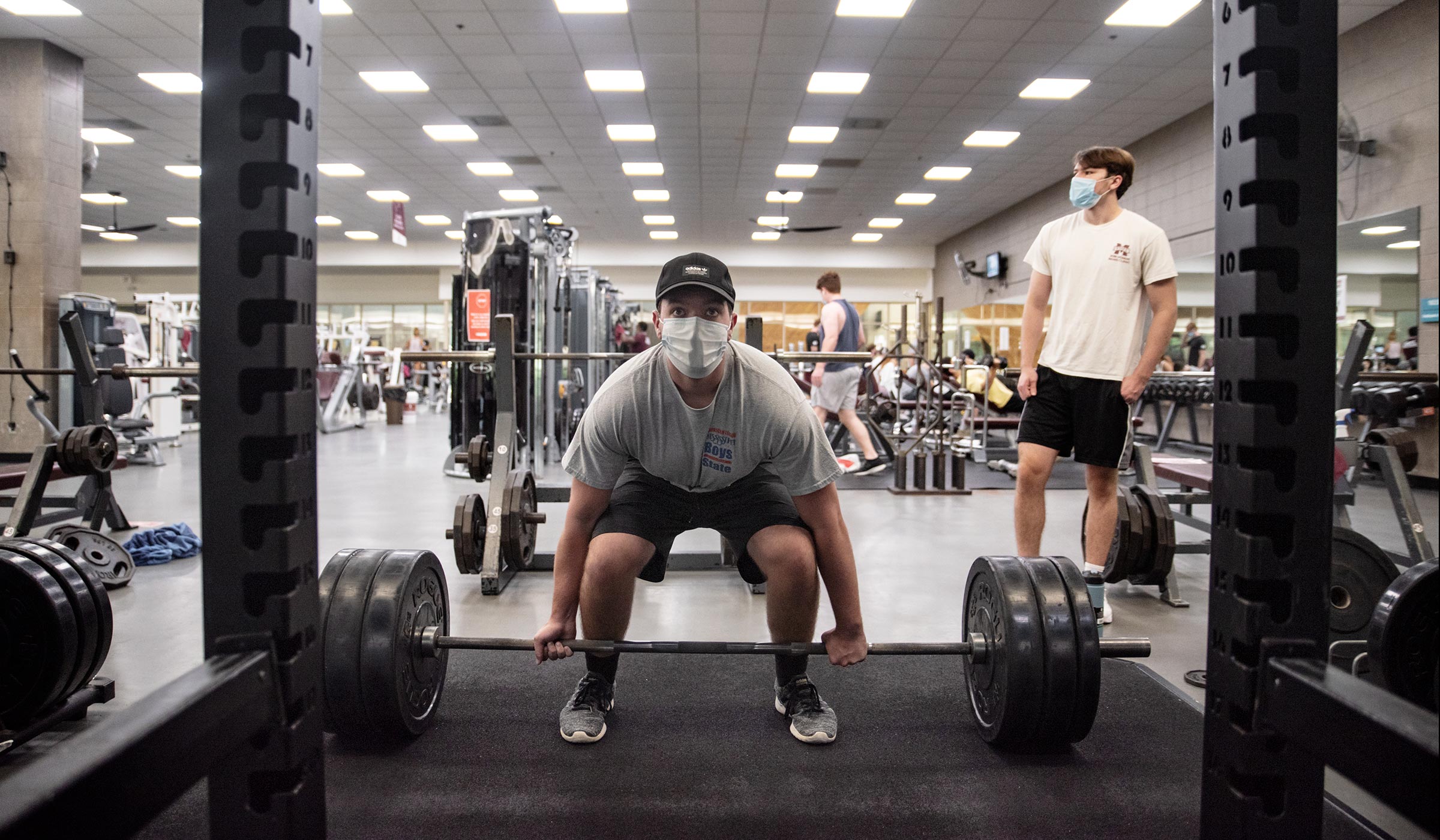 Masked student lifts heavy weights in Sanderson weight room.