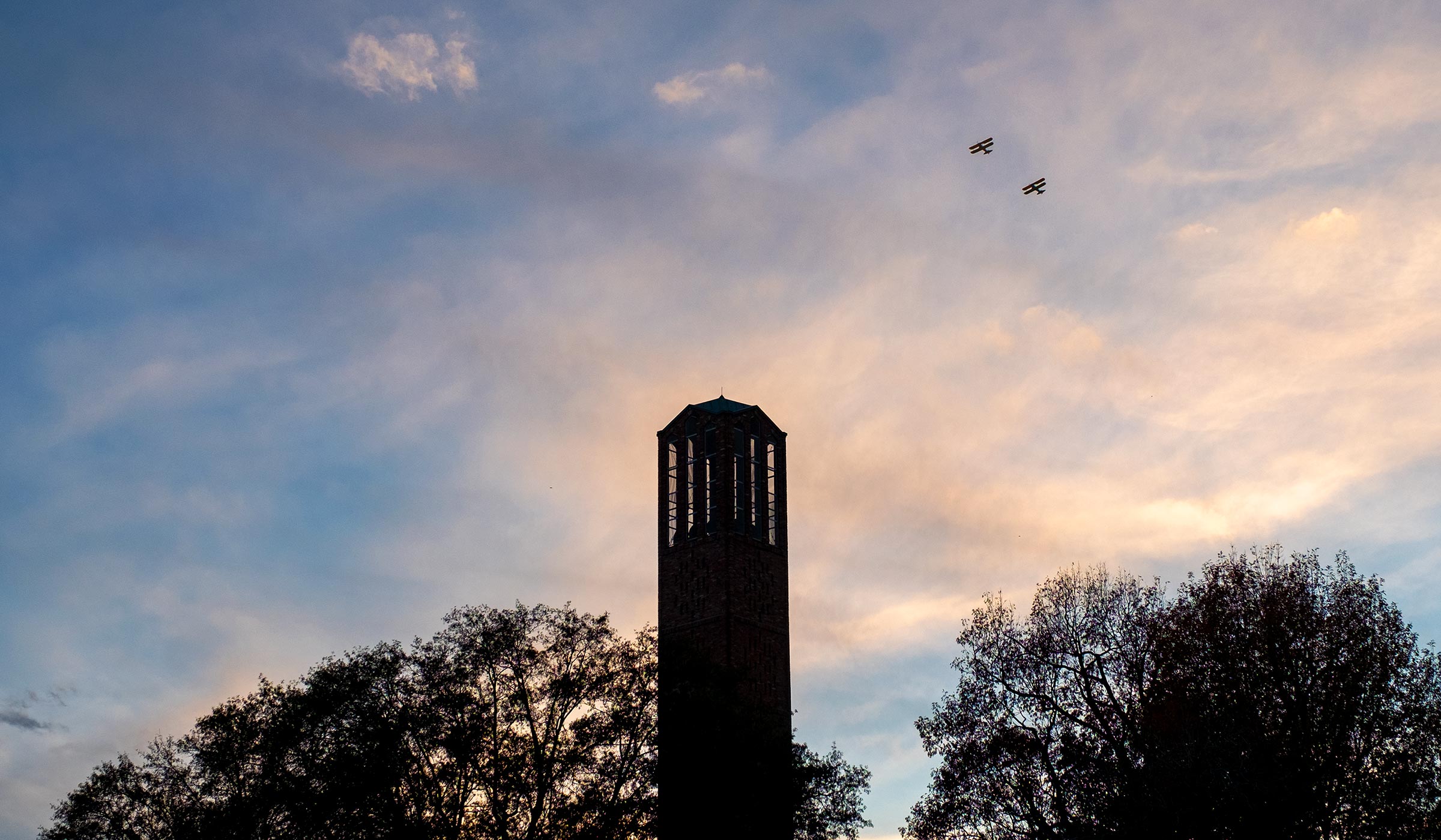 Chapel tower with pair of biplanes against the sunset clouds.
