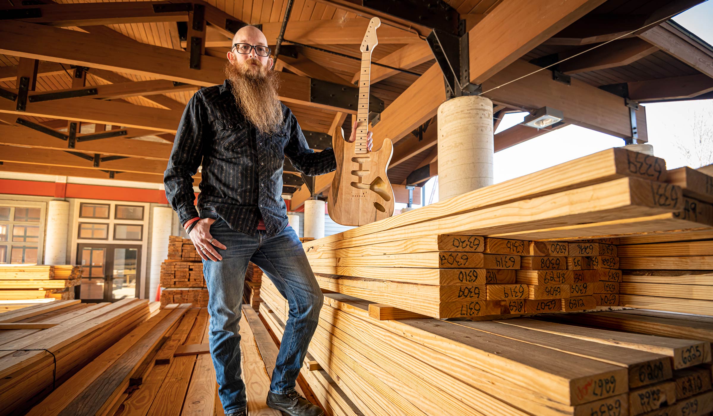 Adam Wade, pictured with a guitar and standing on a pile of lumber.