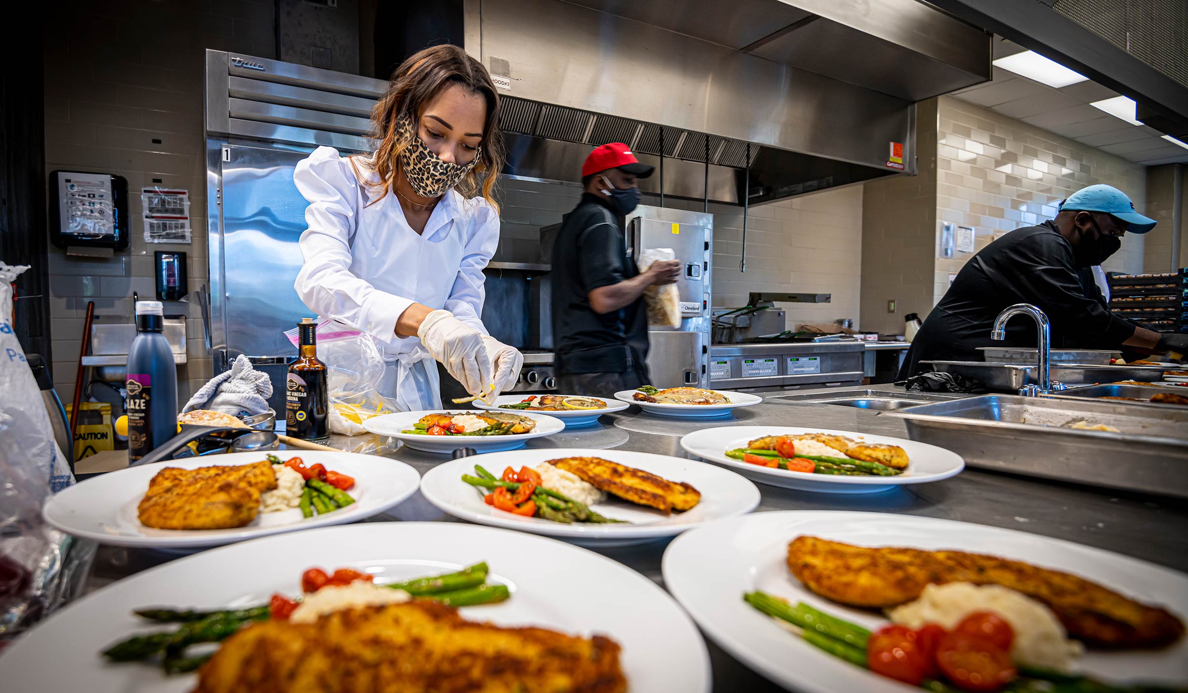 Woman in white shirt, gloves, and mask plating food on white plates