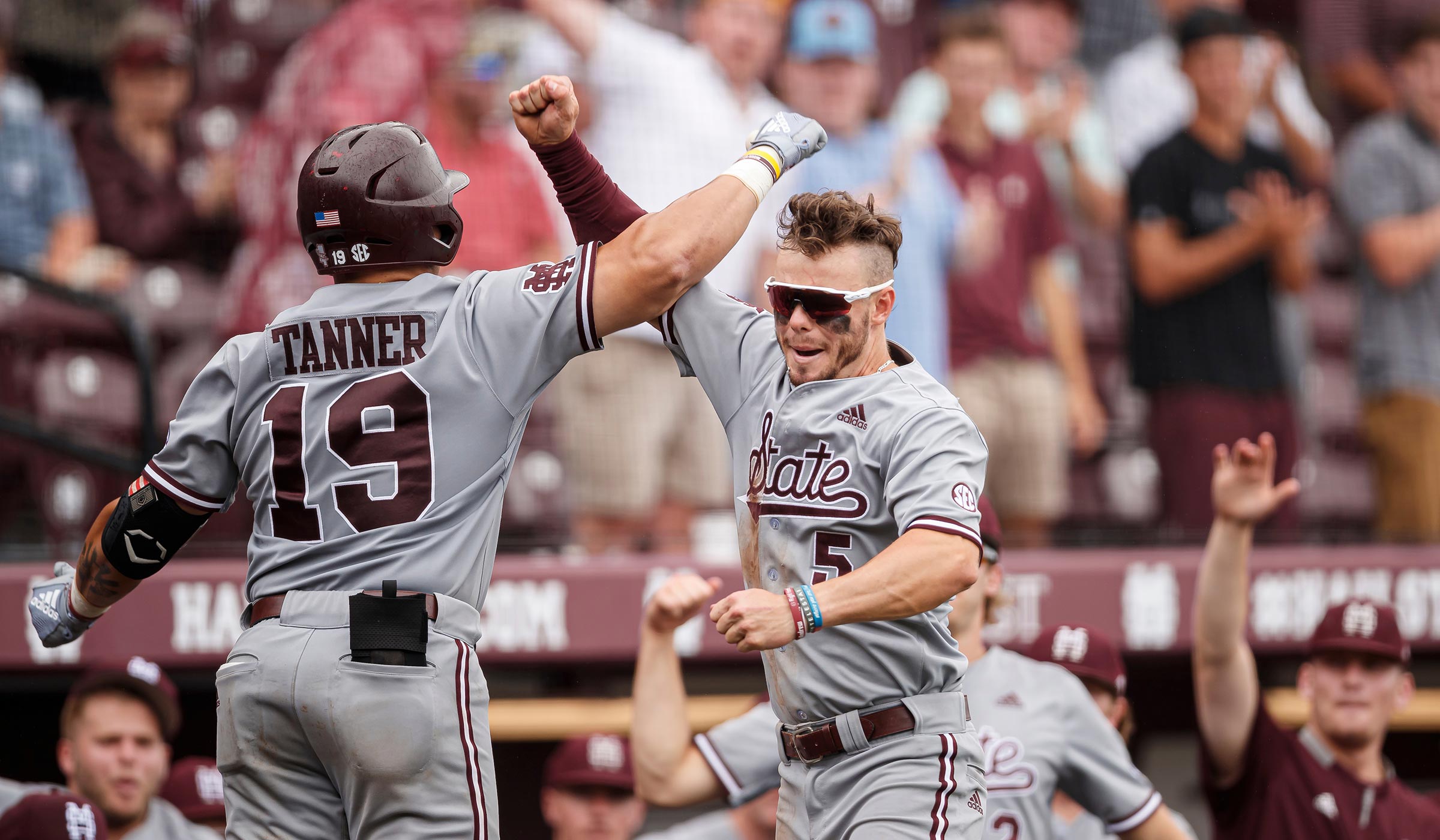 Two baseball players in gray and maroon uniforms jumping and crossing arms