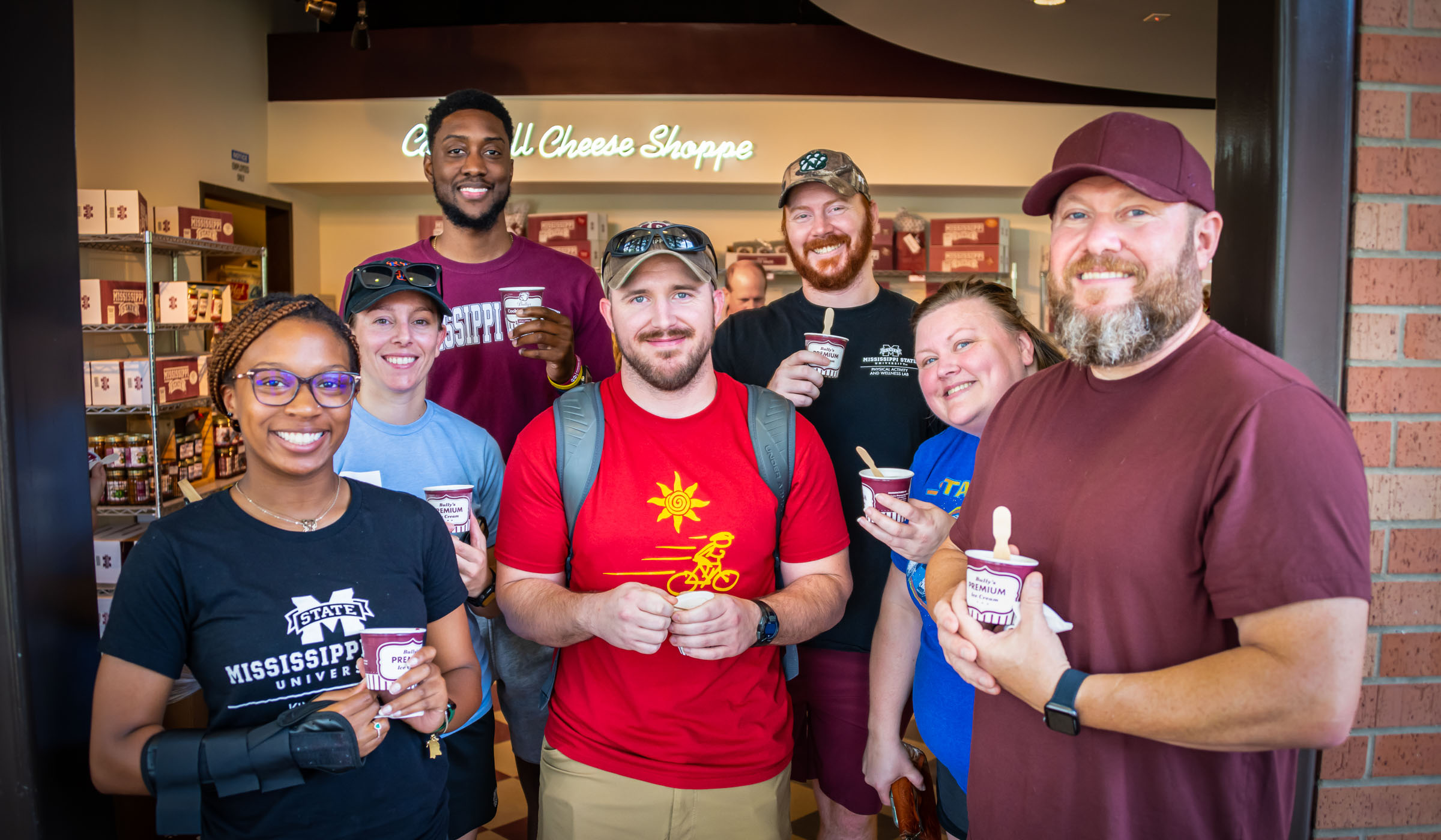 A group of seven MSU employees stand smiling in the door of the MSU Cheese Shop, holding MSU ice cream.