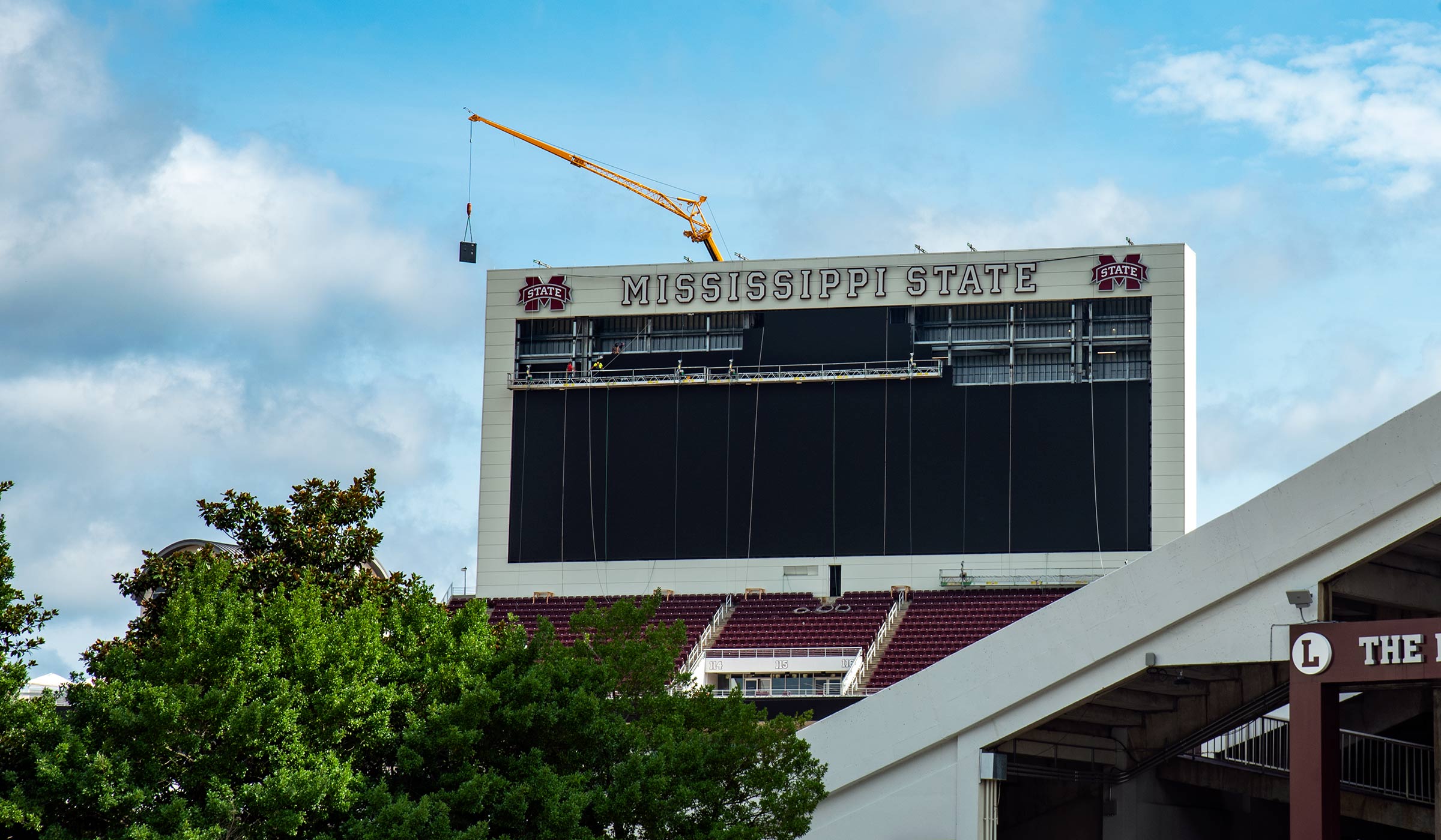 Yellow crane moving screen pieces into place at stadium