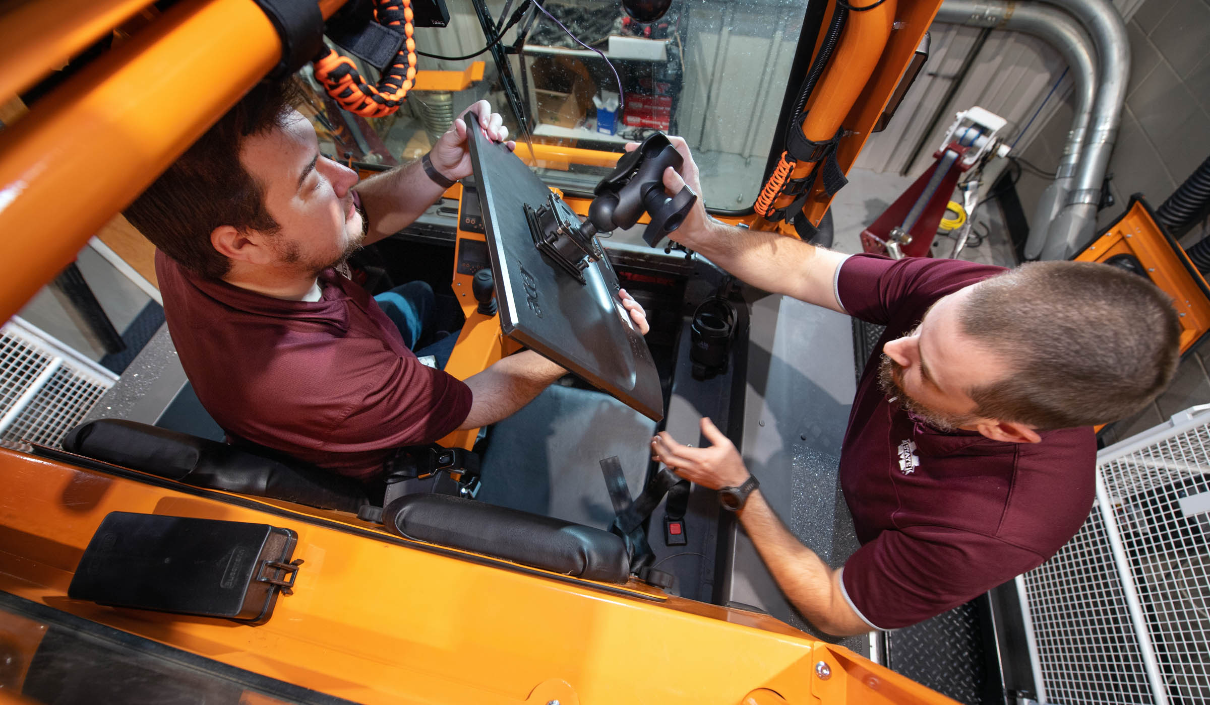 Viewed from above through the roof of the orange off-road vehicle, two CAVS research engineers install a screen inside the windshield..