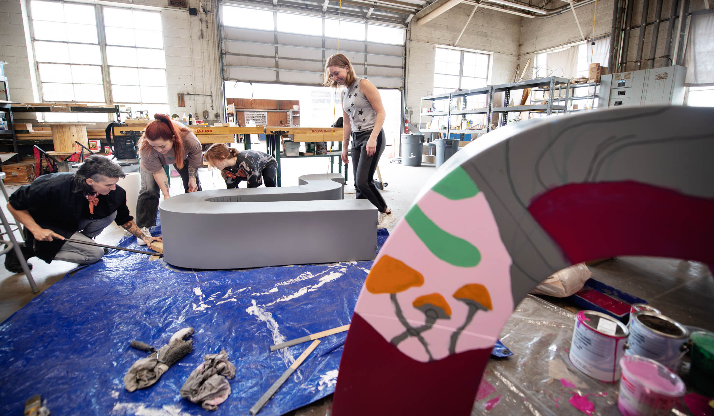 Sculpture professor Professor Caroline Hatfieldand three students raise up one of the curvy metal sculptures for painting, with another partly painted component in the studio foreground.