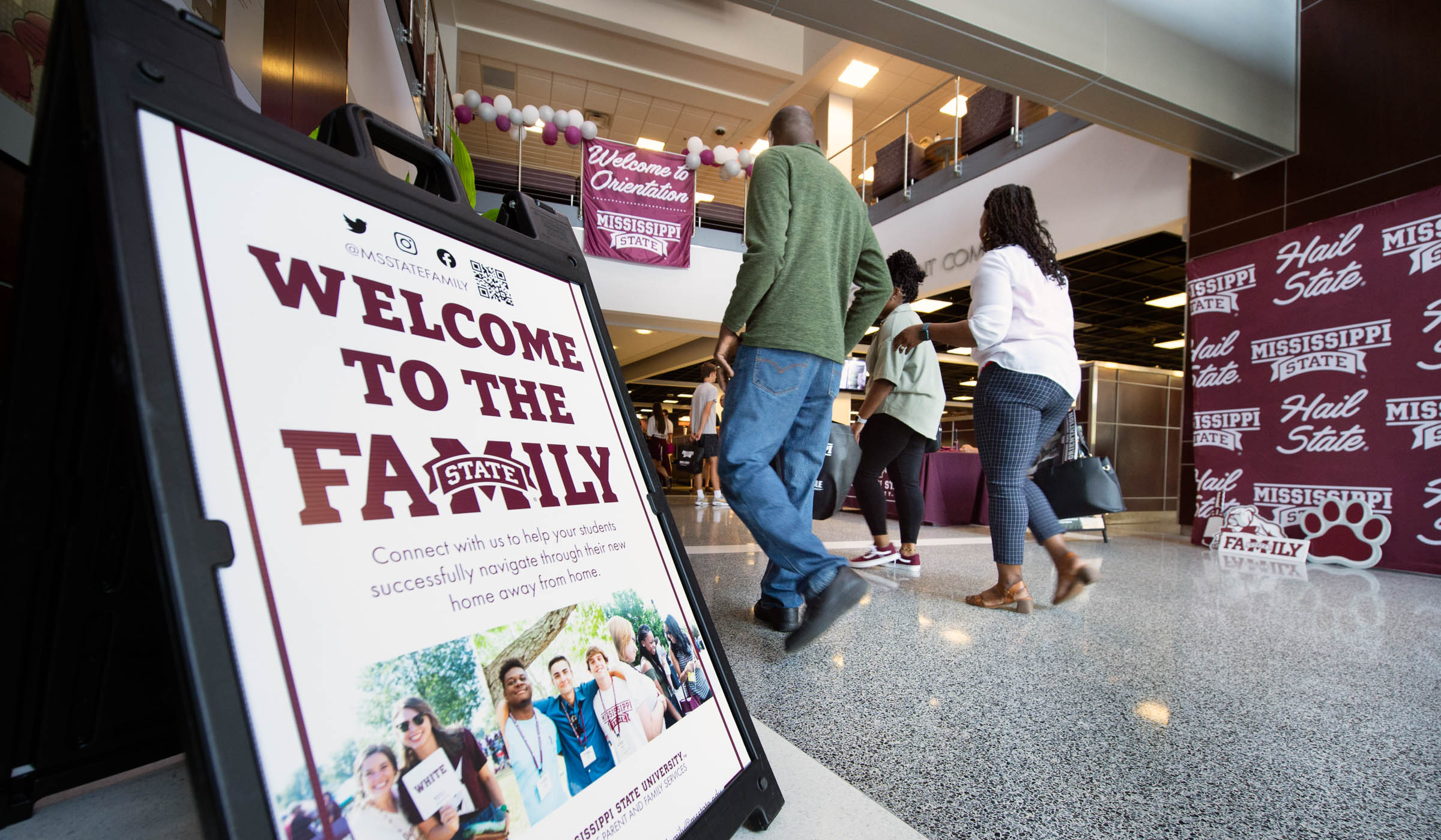 With a Welcome to the Family sign at the left and a Welcome to Orientation sign hanging above, incoming students and their families enter Colvard Union&#039;s hall for Orientation sign-in