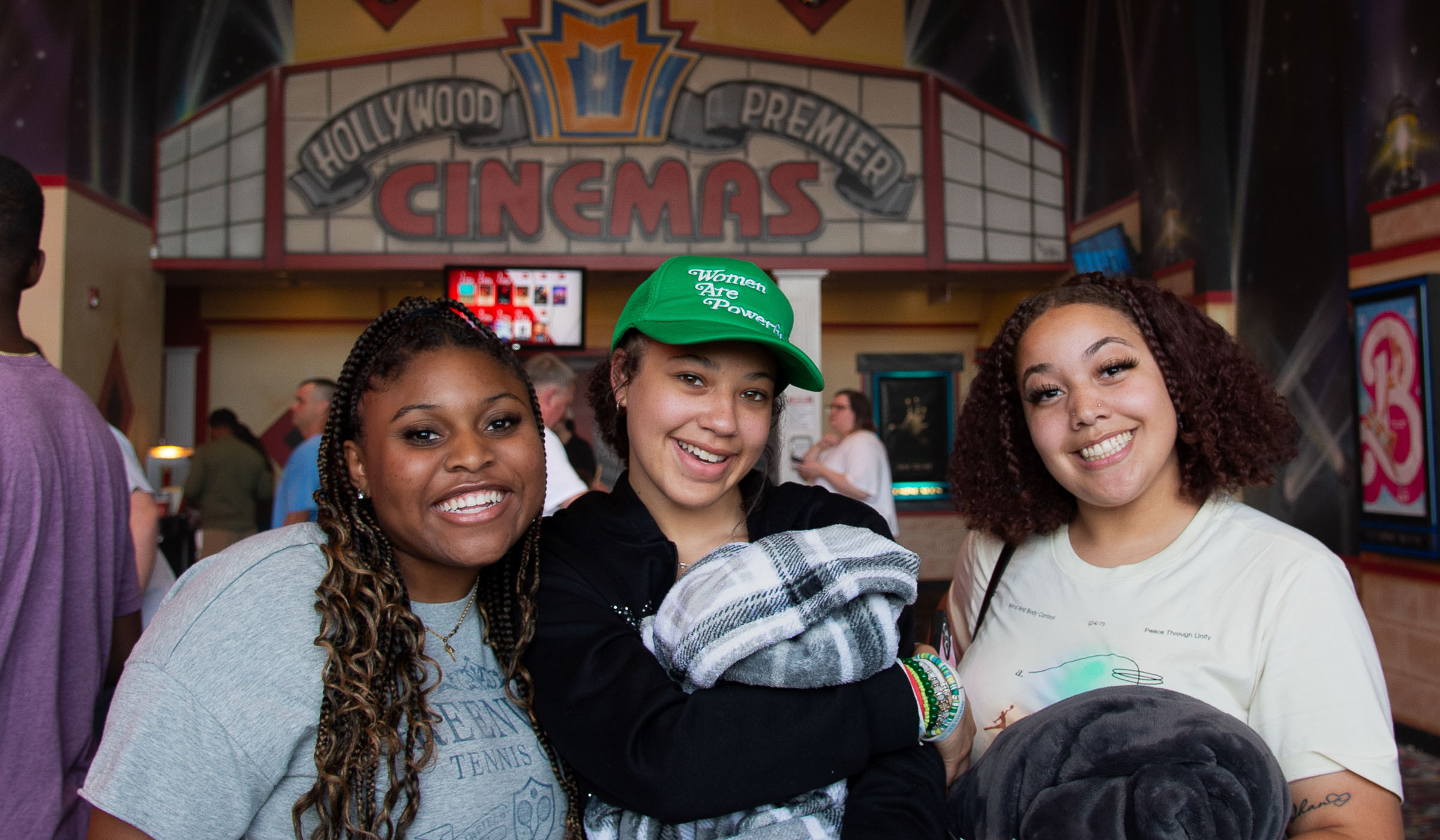 Three College Ready students smile at the camera in the movie theater lobby.