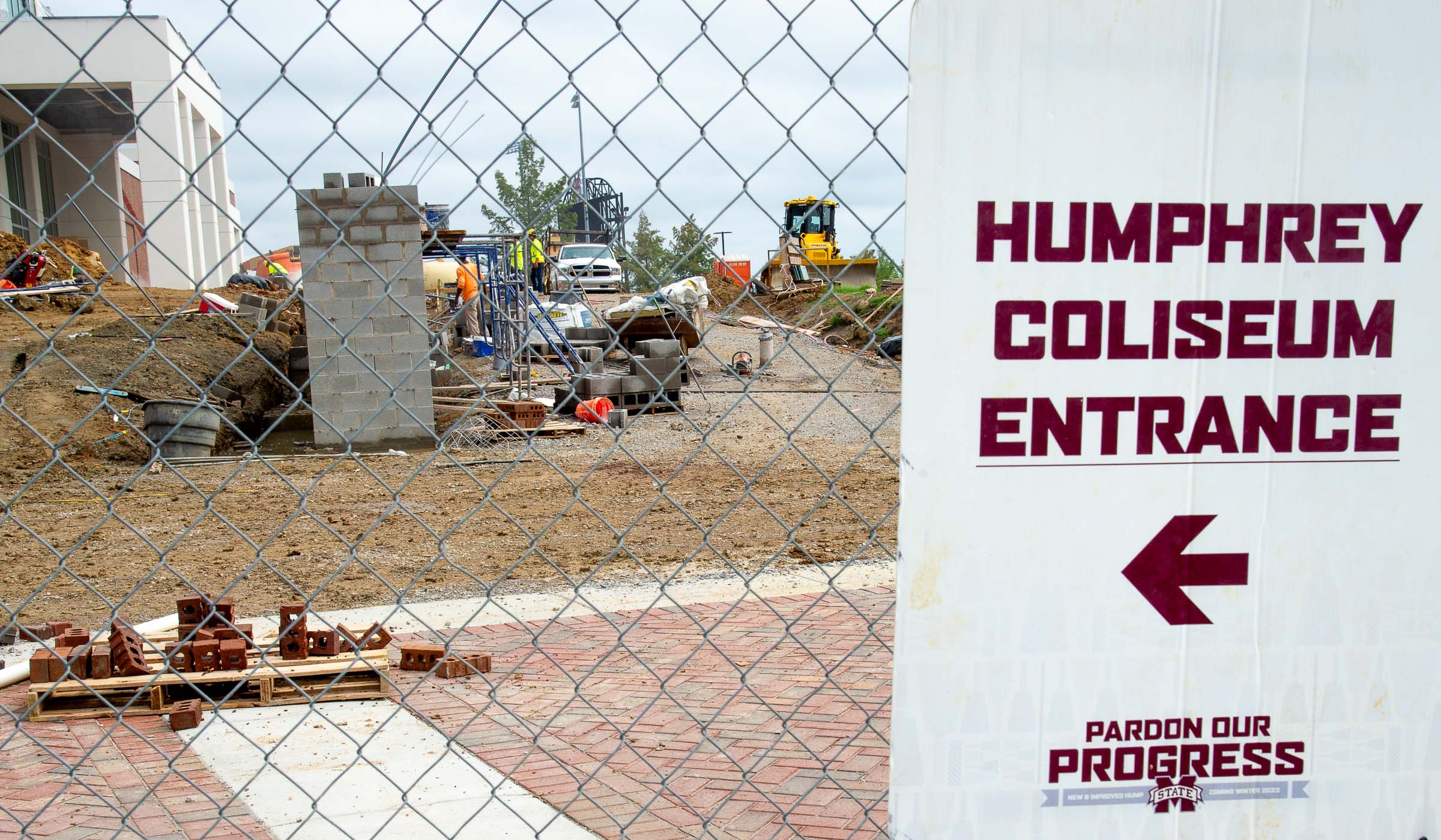 &quot;Pardon Our Progress&quot; sign on fench with construction in the background, with arrow pointing the way to the Humphrey Coliseum Entrance.
