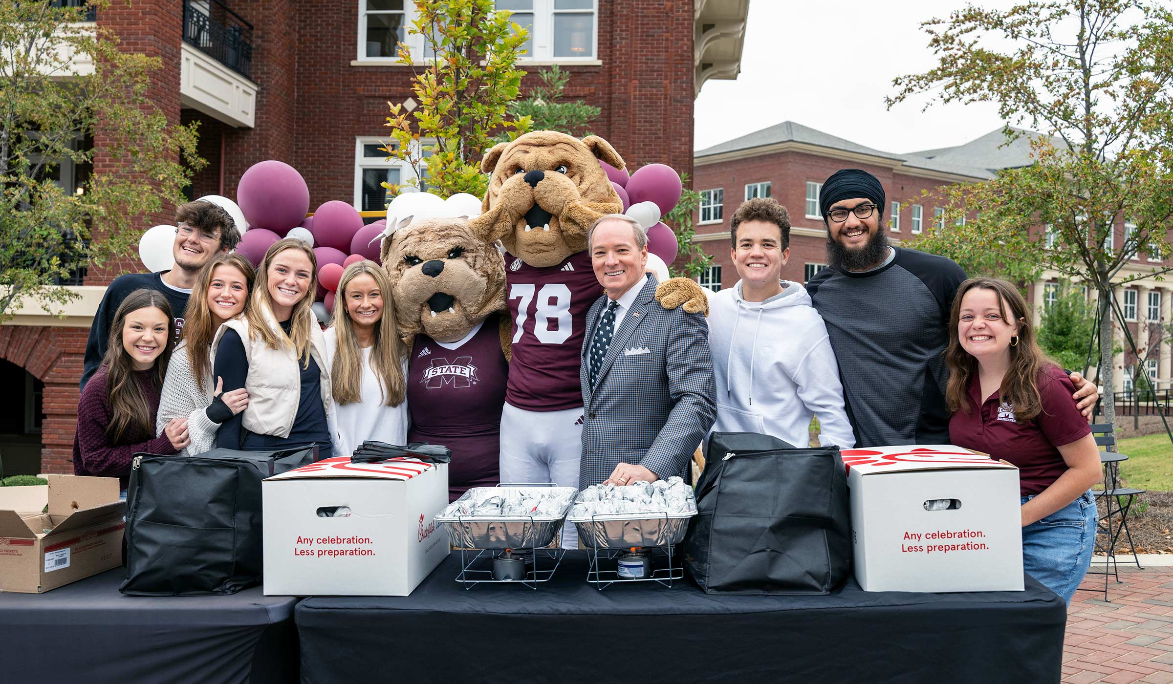 Group of people with two bulldog costume mascots with table in front of them with food to hand out.