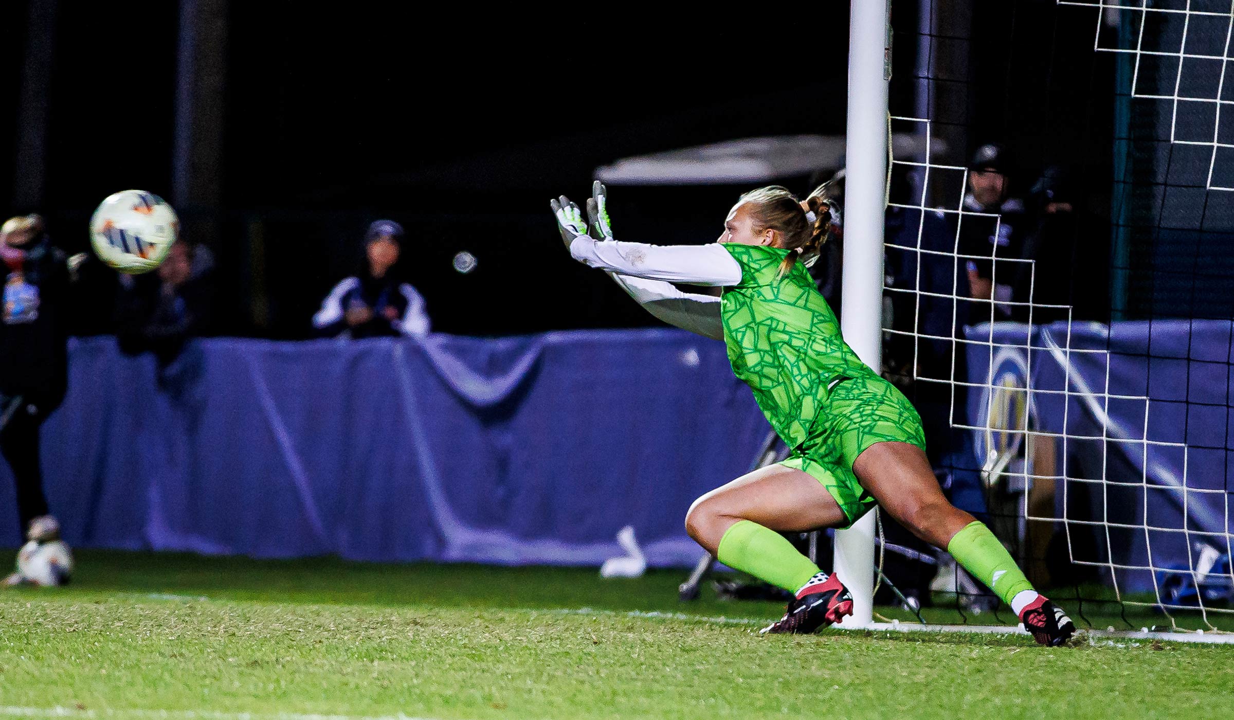 Female goalkeeper in green soccer kit diving towards soccer ball