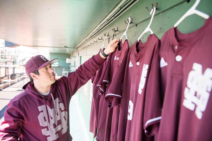 Baseball manager hanging maroon jerseys in the dugout at Dudy Noble.