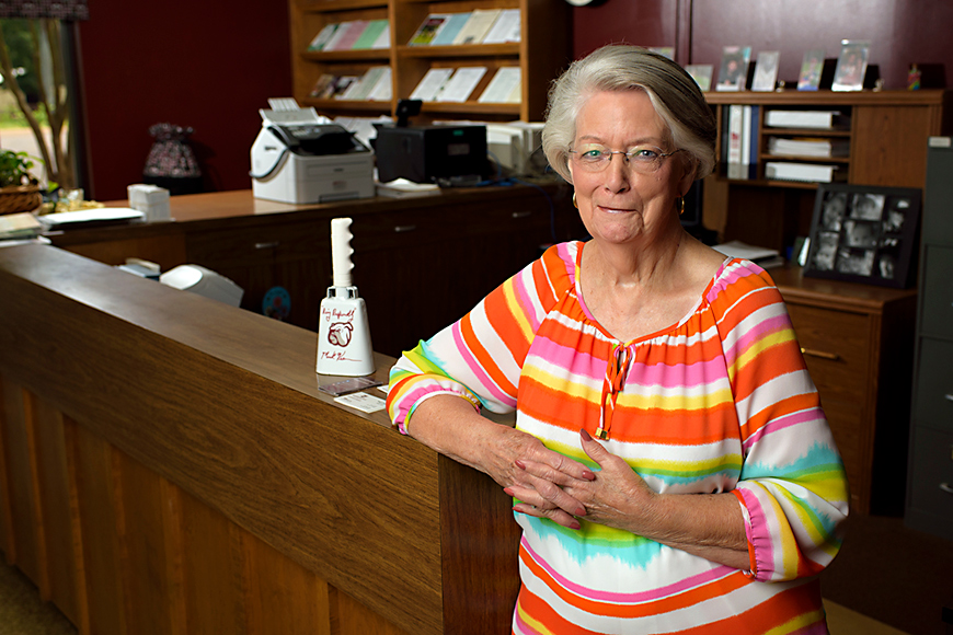 Nancy Bearden stands in front of a desk with a white cowbell to her left.