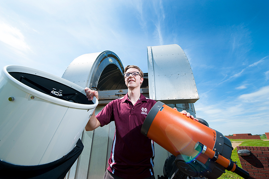 Randy Niffengger poses with astronomy equipment with a blue sky in the background.