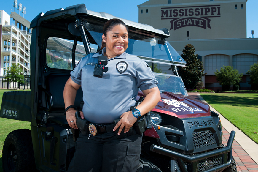 Chantel Solis stands in uniform in front of a university police vehicle near the stadium.