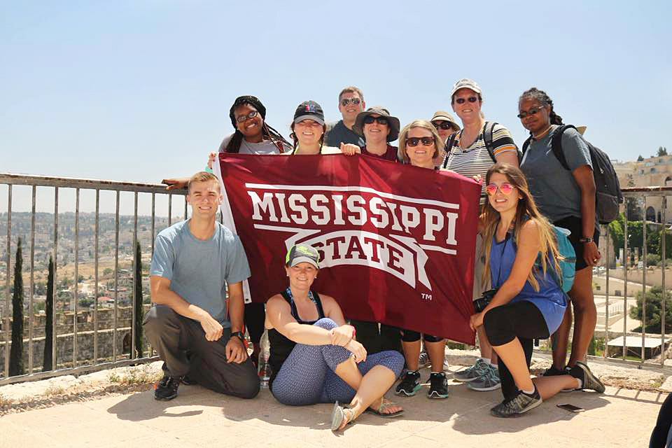 Group of scholars holding maroon Mississippi State flag overlooking landscape in Israel.