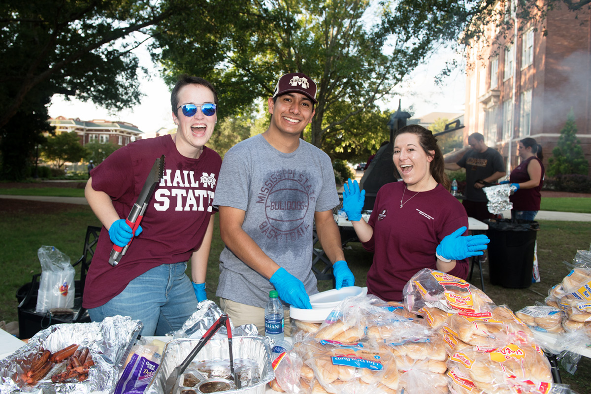 Students laughing together while waiting to hand out more hot dogs and hamburgers on the Drill Field