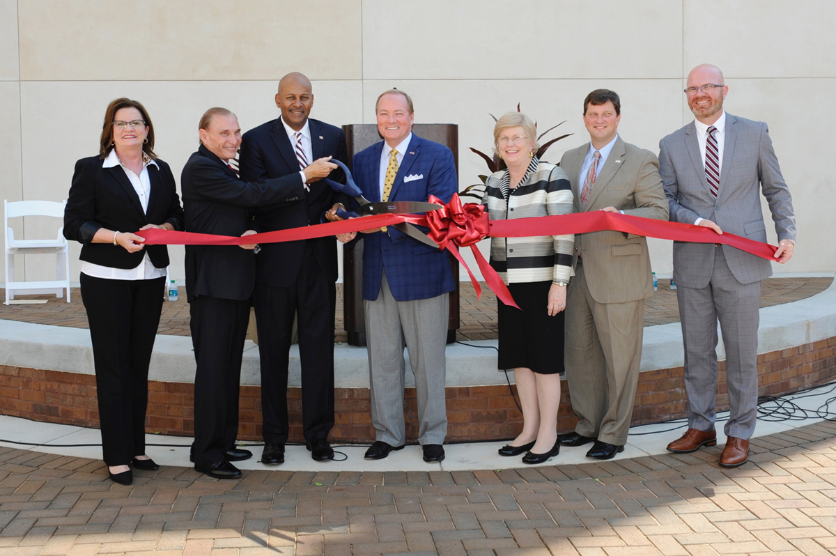Public figures from Starkville and Meridian campus use giant scissors to cut a ribbon on a new plaza in Meridian.