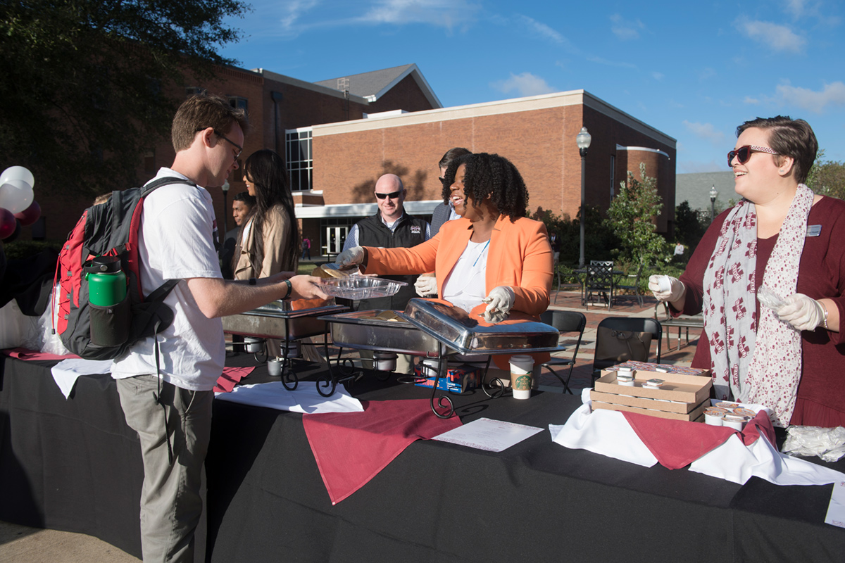 Female staff member in orange jacket serving pancake to student on the Drill Field