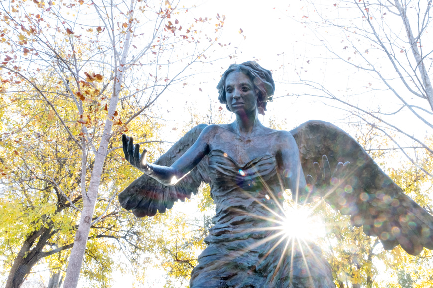 The Chapel&amp;#039;s bronze angel sculpture with afternoon sun flare and fall leaves behind
