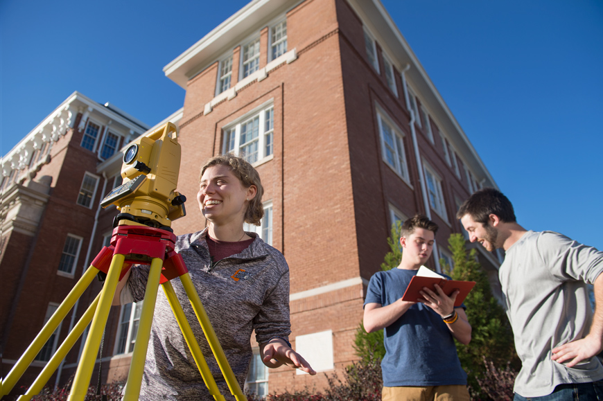 Team of three students complete class surveying assignment next to Lee Hall.