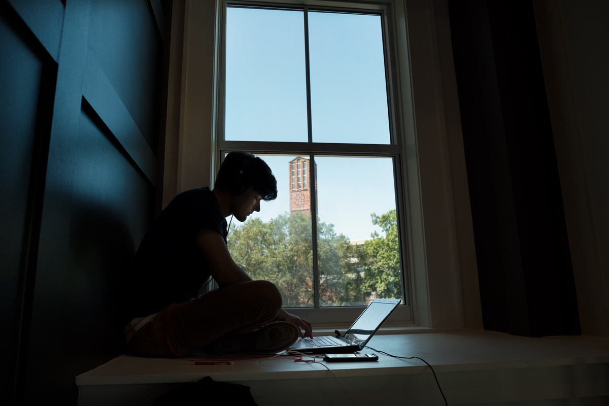 Framed by a view of the Chapel tower, a student works on his laptop on a window seat.