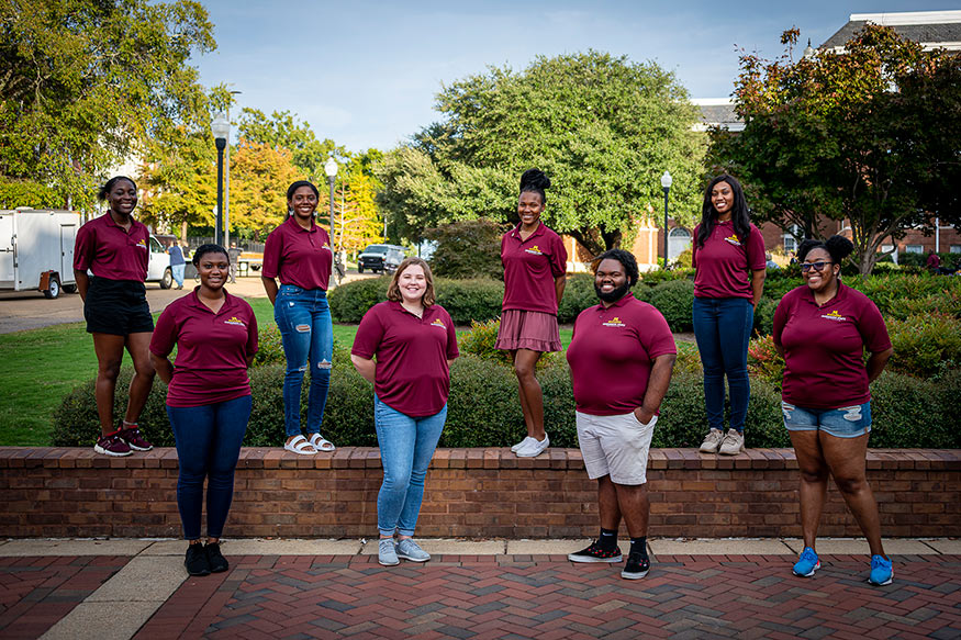 Eight students dressed in their maroon MANRRS shirts, stand near MSU's Colvard Student Union.