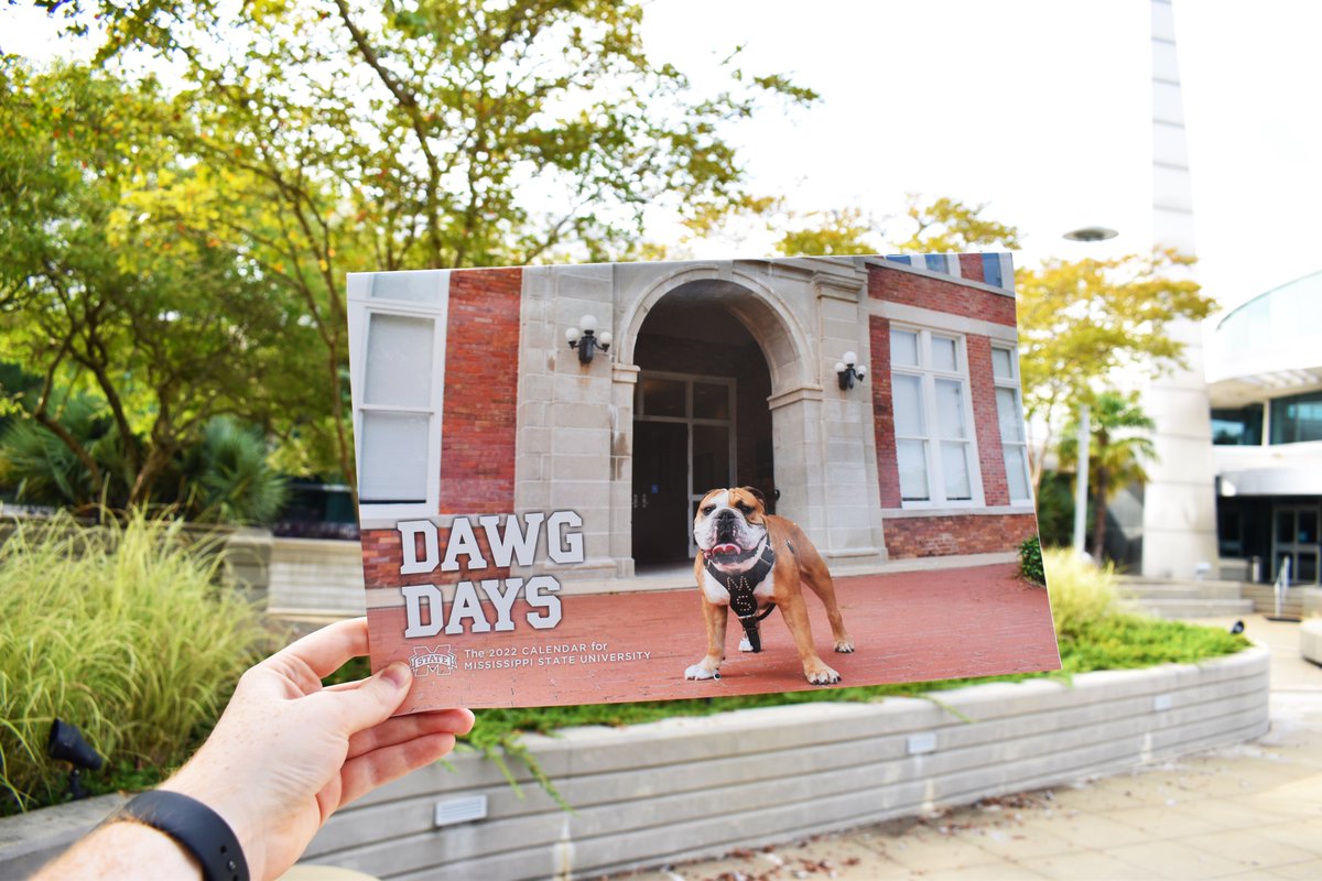 A person holds up the 2022 MSU Dawg Days calendar in front of the Hunter Henry Center
