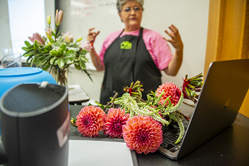 Bright pink flowers are pictured resting on an Apple computer while MSU floral management instructor Lynette Dougald stands in the background.