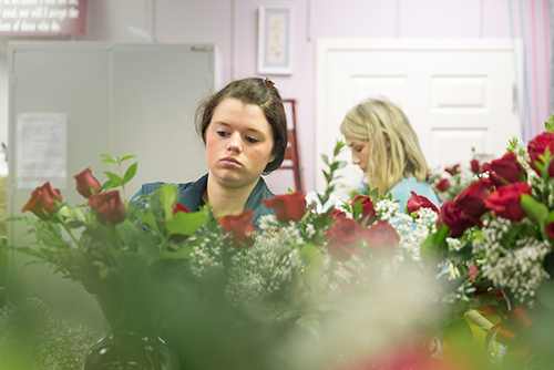 Two female students arrange roses at the University Florist.