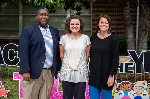 Lawhon Elementary School Principal Ian Shumpert, Mississippi Teacher of the Year Leslie Tally and Lawhon Assistant Principal Kama Smith take a group photo in front of a yard sign of letters.