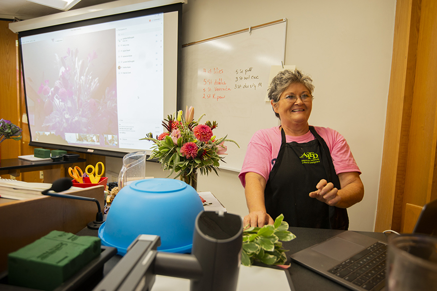 MSU floral management instructor Lynette McDougald smiles while standing near a bouquet of bright pink flowers in a classroom.