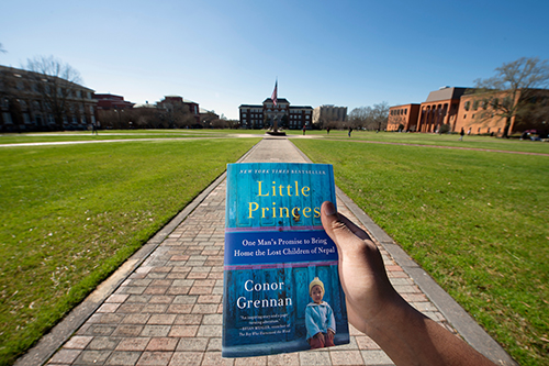 2020 Maroon Edition book, “Little Princes: One Man’s Promise to Bring Home the Lost Children of Nepal,” held by student on the Drill Field