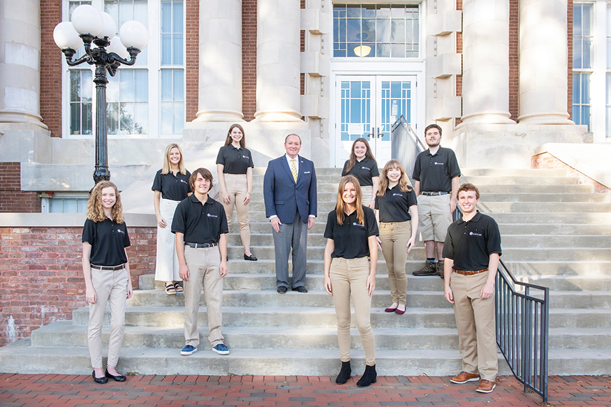 MSU President Mark E. Keenum and the university's newest Presidential Scholars smile while standing on the front steps of Lee Hall.