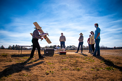 Amelia Fox (far left), assistant clinical professor in the MSU Department of Plant and Soil Sciences, readies the fixed-wing E-flite Timber Apprentice for flight while students and colleagues look on. 