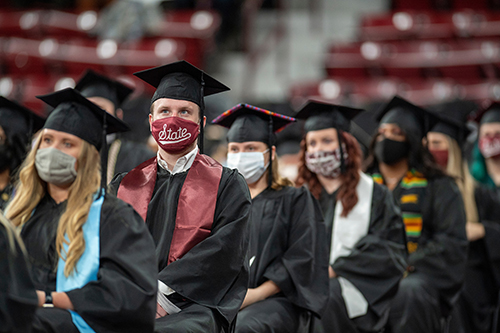 MSU graduates are seated in Humphrey Coliseum wearing graduation caps and gowns, as well as face coverings.