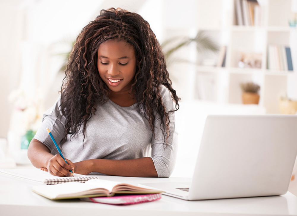 An African-American girl with long hair studies in front of her computer