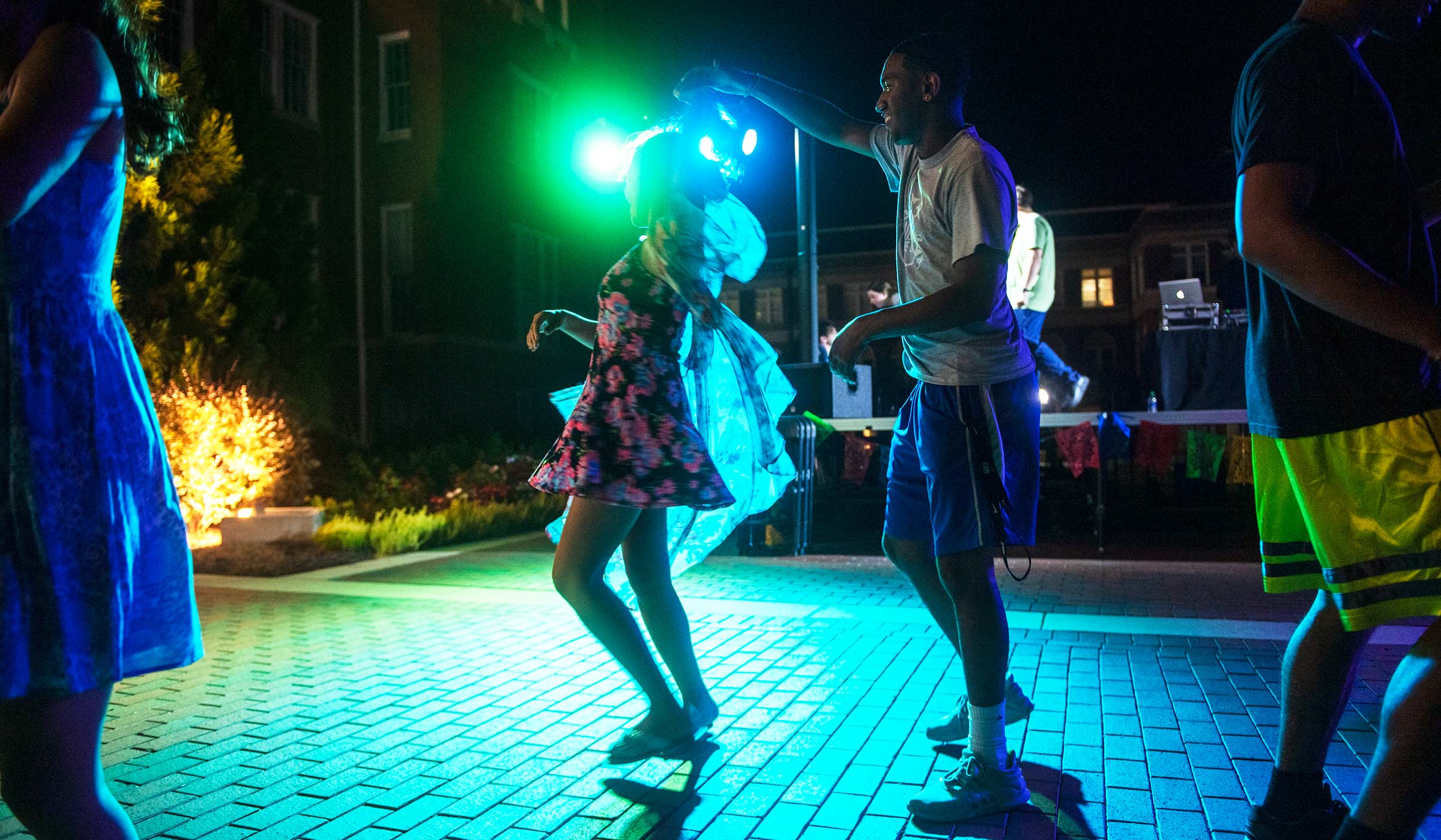 Male student twirling female student in dance move in front of stage with lights on brick plaza