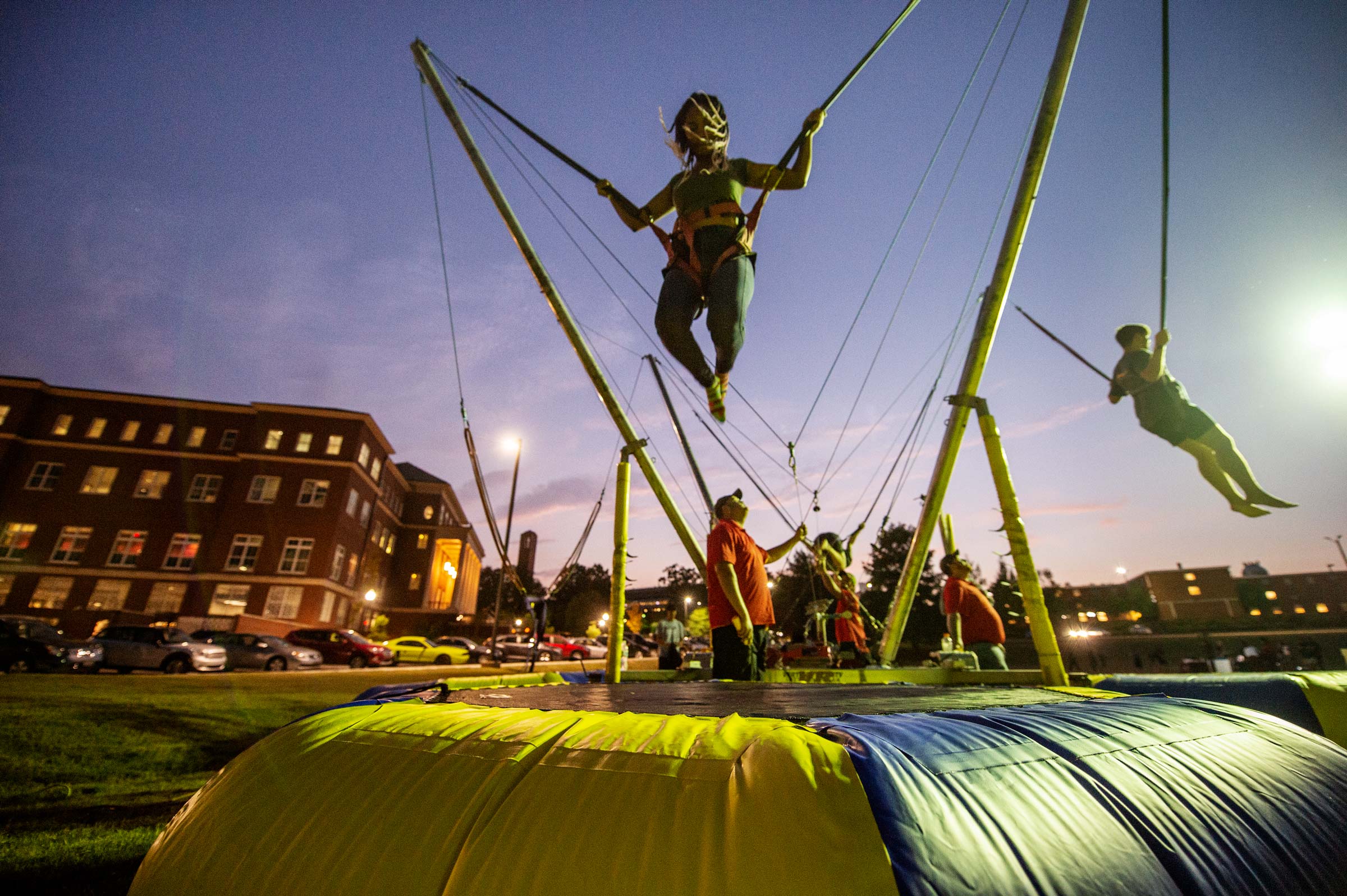 Student catching air on a bouncy jumper, with the dusky sky and old Main Academic Center.