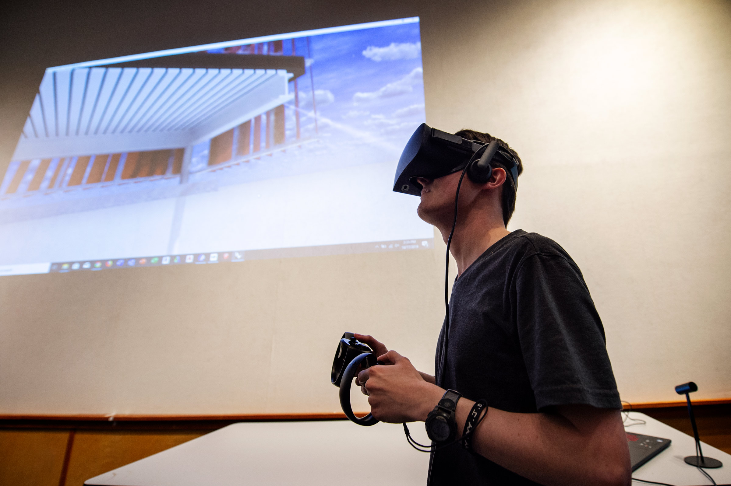 With virtual reality glasses and controls, Architecture student Matthew Churchill tours a 3D rendering of his design with his view projected behind him.