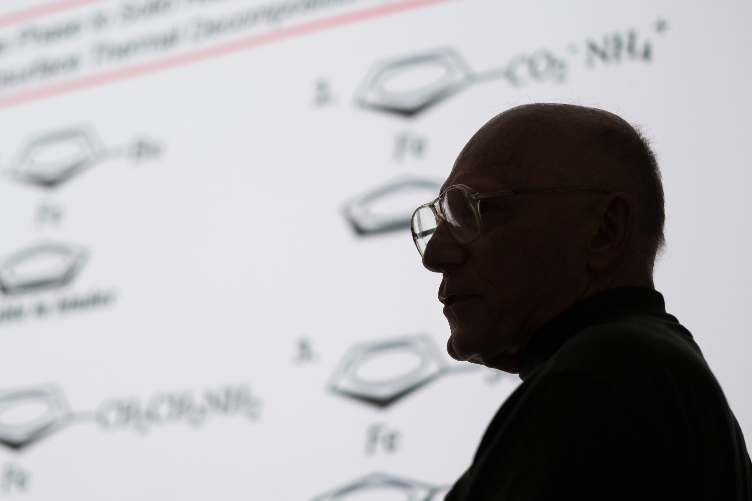 Emeritus Professor Pittman&#039;s profile in silhouette with chemistry diagrams projected behind him.