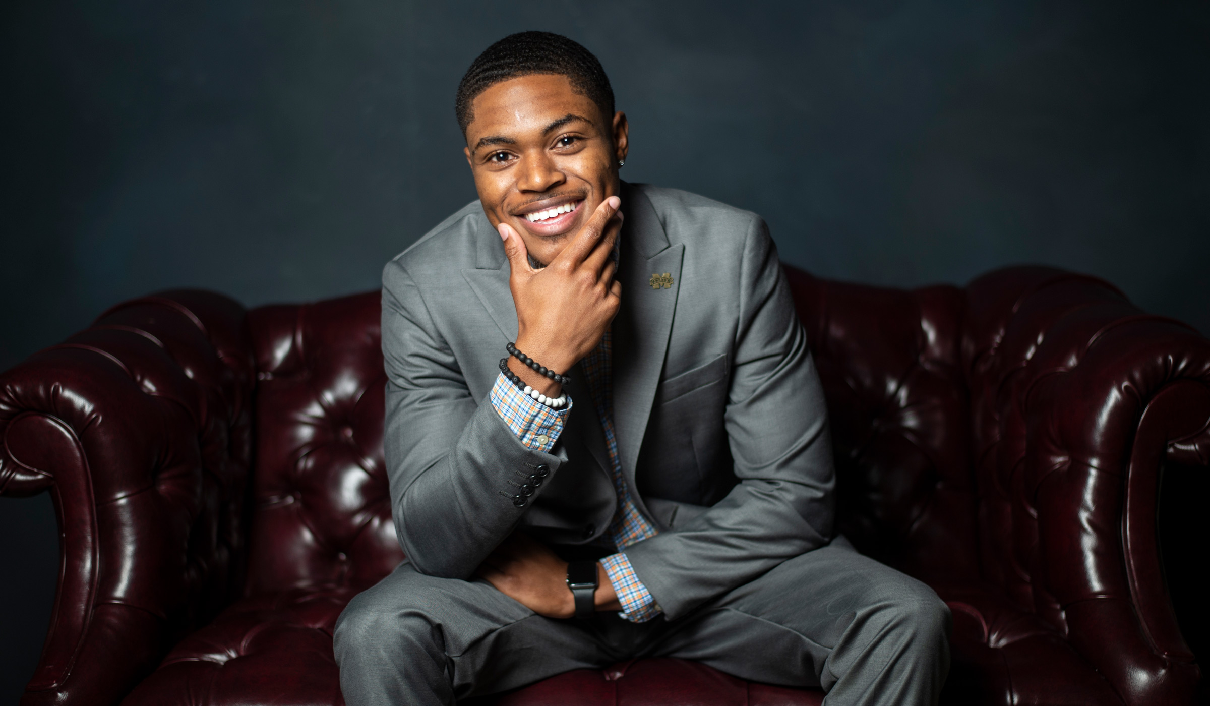 Caleb Jenkins, pictured on a leather couch in a photo studio.