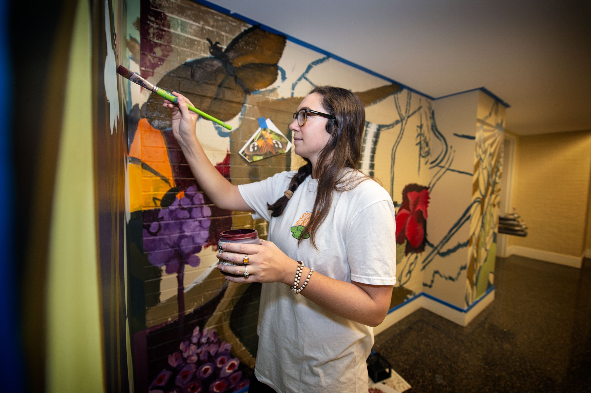 Art student Ronni Brashear paints a Harned hallway wall with butterflies and other subjects of Biological Sciences departmental research.