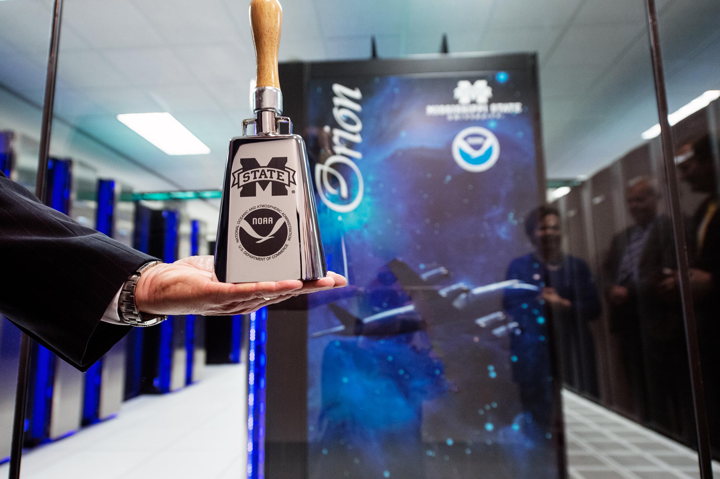 NOAA&#039;s Craig McLean holds cowbell in front of Orion supercomputers in HPCC.