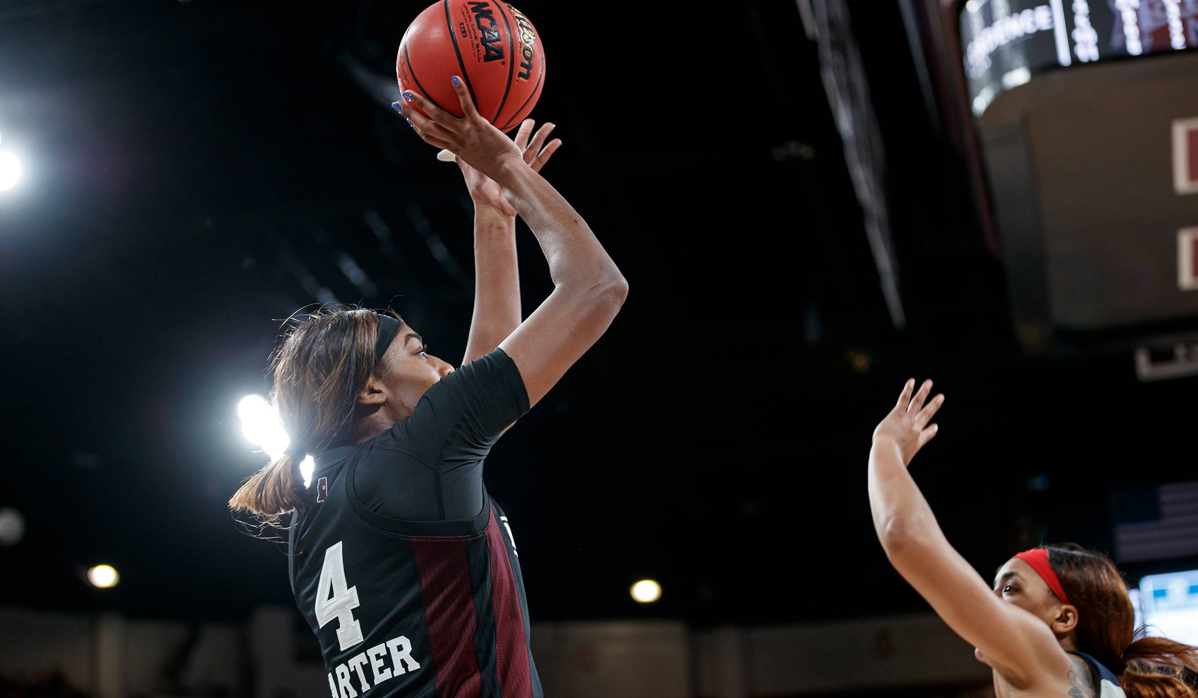 Women&#039;s basketball player in black uniform shooting the ball over opponents&#039; head.