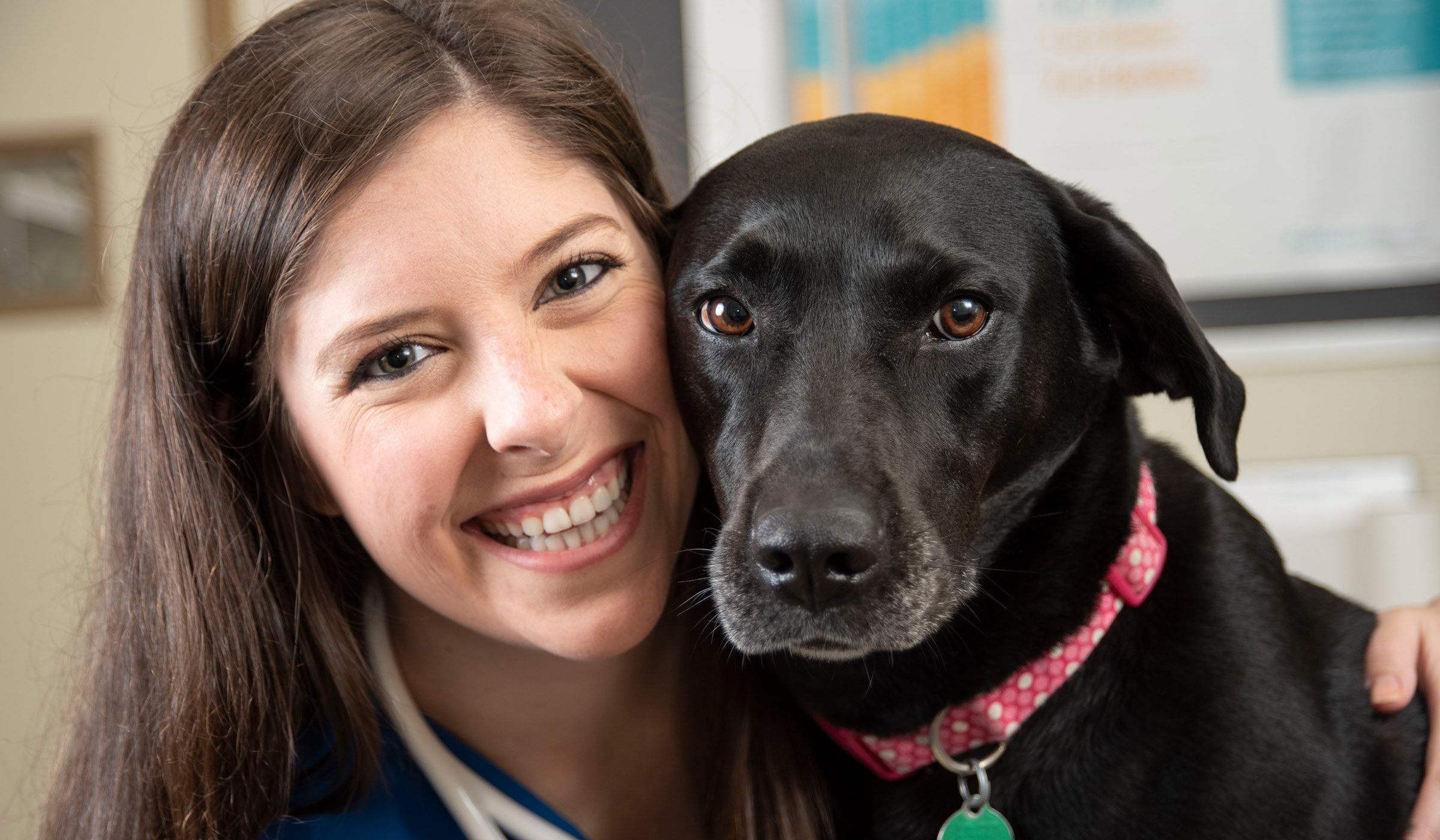 A young woman smiles as she hugs a black dog