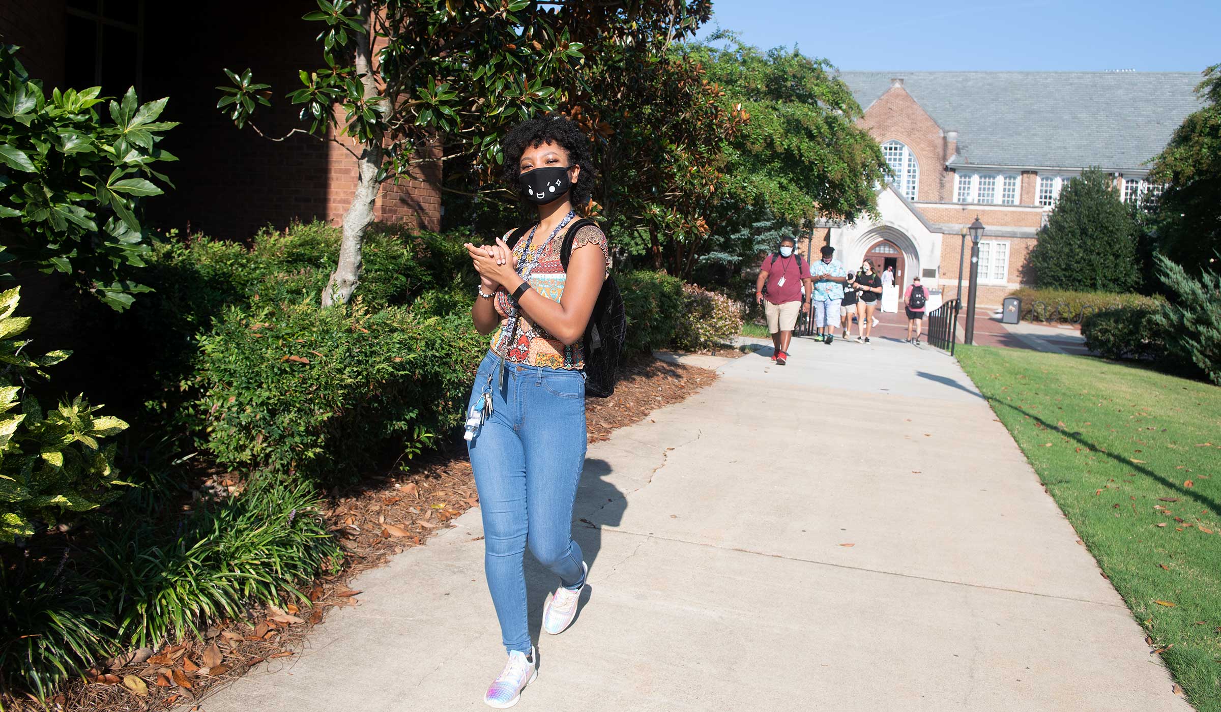 Female student walking ahead of crowd on sidewalk with mask on.